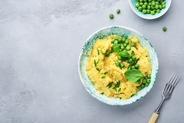 Mashed potato with butter, green peas, onions, basil in a white bowl