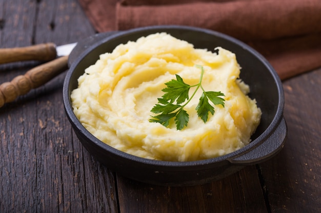 Photo mashed potatoes or boiled puree with parsley  in cast iron pot on dark wooden rustic surface .