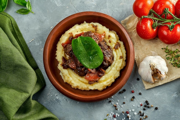 Mashed potatoes with stewed meat in a clay dish on a concrete background