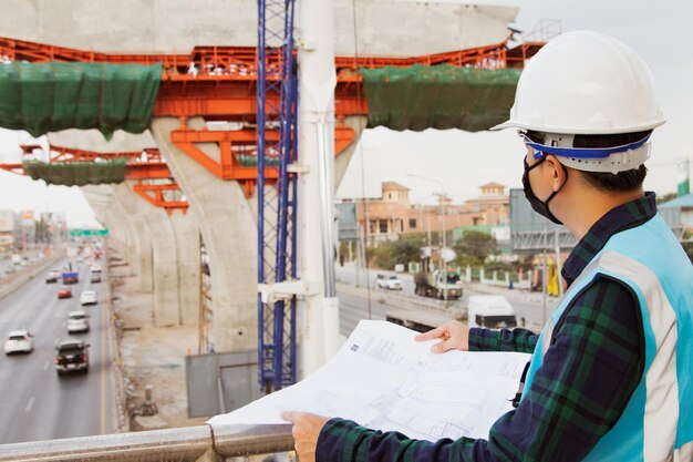 Masked asian architect and engineer monitor the progress road construction project linking the city