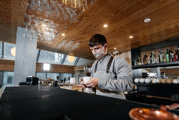 A masked barista exquisitely serves readymade coffee in a modern cafe during a pandemic Serving readymade coffee to a client in a cafe