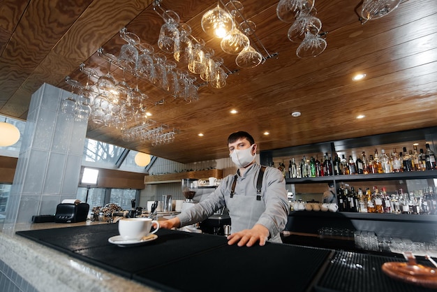 A masked barista exquisitely serves readymade coffee in a modern cafe during a pandemic Serving readymade coffee to a client in a cafe