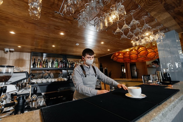 A masked barista exquisitely serves readymade coffee in a modern cafe during a pandemic Serving readymade coffee to a client in a cafe