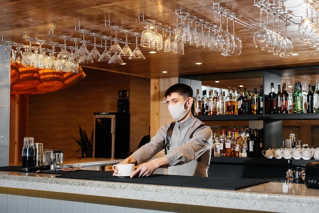 A masked barista exquisitely serves readymade coffee in a modern cafe during a pandemic Serving readymade coffee to a client in a cafe