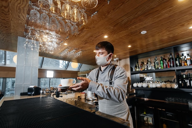 A masked barista exquisitely serves readymade coffee in a modern cafe during a pandemic Serving readymade coffee to a client in a cafe