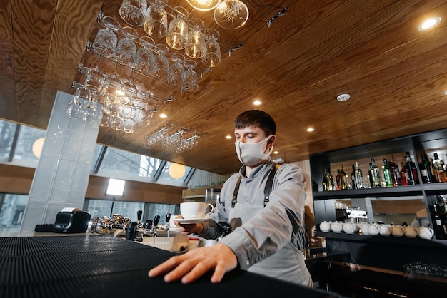 A masked barista exquisitely serves readymade coffee in a modern cafe during a pandemic Serving readymade coffee to a client in a cafe