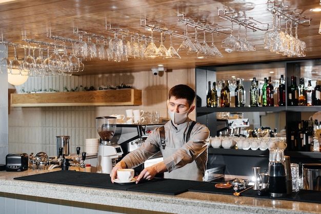 A masked barista exquisitely serves readymade coffee in a modern cafe during a pandemic Serving readymade coffee to a client in a cafe