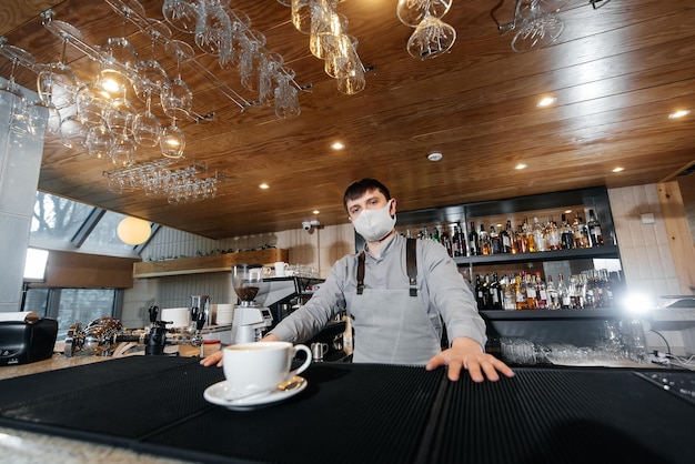 A masked barista exquisitely serves readymade coffee in a modern cafe during a pandemic Serving readymade coffee to a client in a cafe