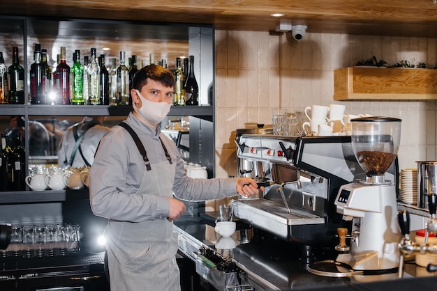 A masked barista prepares delicious coffee at the bar in a cafe. The work of restaurants and cafes during the pandemic.