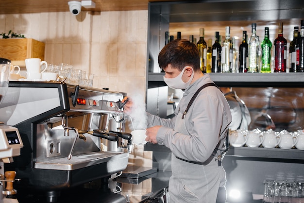 A masked barista prepares delicious coffee at the bar in a cafe. The work of restaurants and cafes during the pandemic.