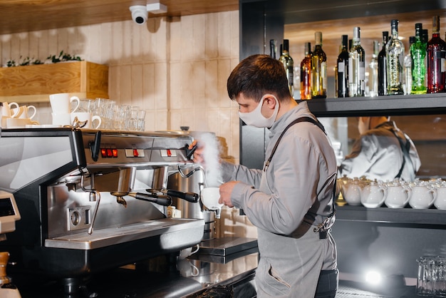 A masked barista prepares delicious coffee at the bar in a cafe. The work of restaurants and cafes during the pandemic.