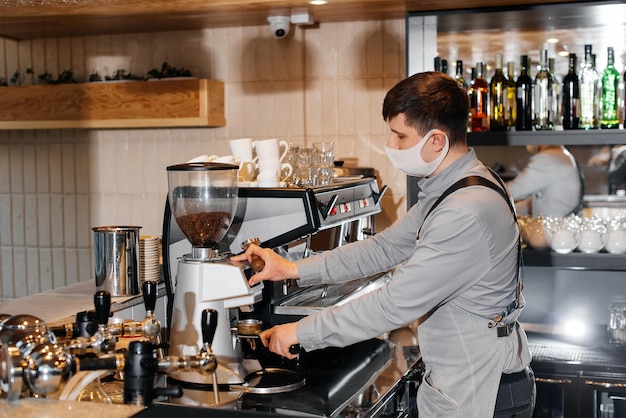 A masked barista prepares an exquisite delicious coffee at the bar in a coffee shop The work of restaurants and cafes during the pandemic