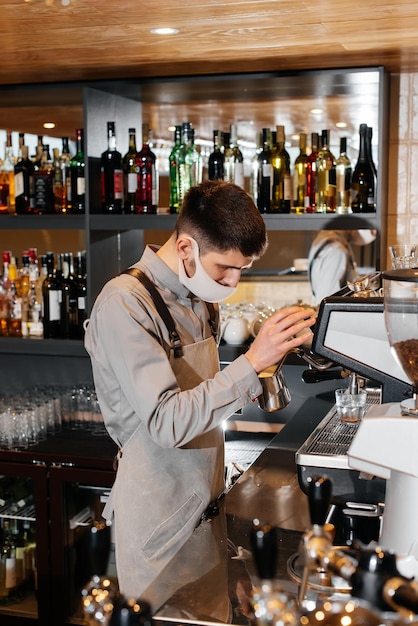 A masked barista prepares an exquisite delicious coffee at the bar in a coffee shop The work of restaurants and cafes during the pandemic