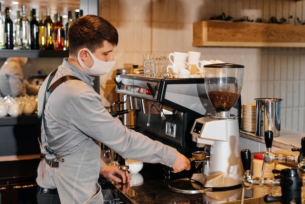 A masked barista prepares an exquisite delicious coffee at the bar in a coffee shop The work of restaurants and cafes during the pandemic