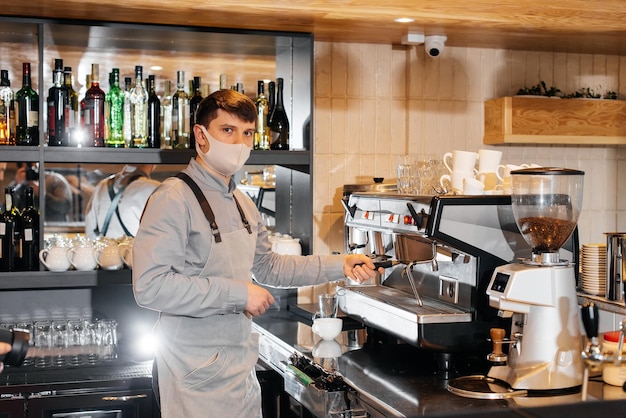 A masked barista prepares an exquisite delicious coffee at the bar in a coffee shop The work of restaurants and cafes during the pandemic