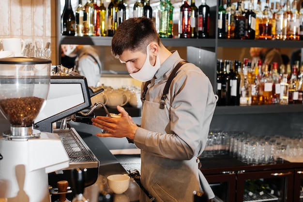 A masked barista prepares an exquisite delicious coffee at the bar in a coffee shop The work of restaurants and cafes during the pandemic