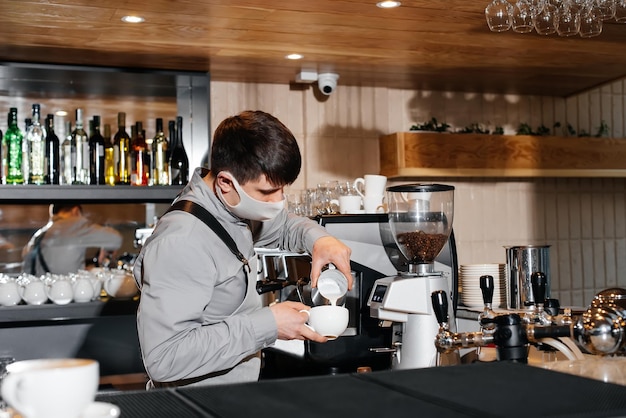 A masked barista prepares an exquisite delicious coffee at the bar in a coffee shop The work of restaurants and cafes during the pandemic