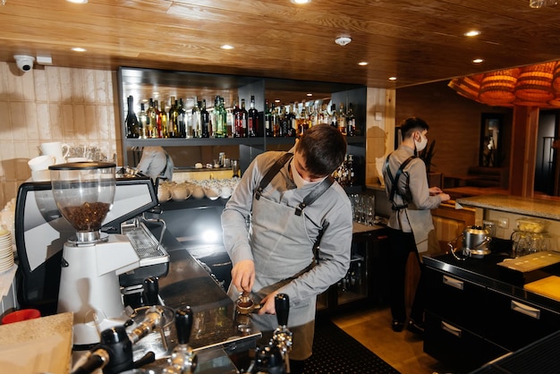 A masked barista prepares an exquisite delicious coffee at the bar in a coffee shop The work of restaurants and cafes during the pandemic