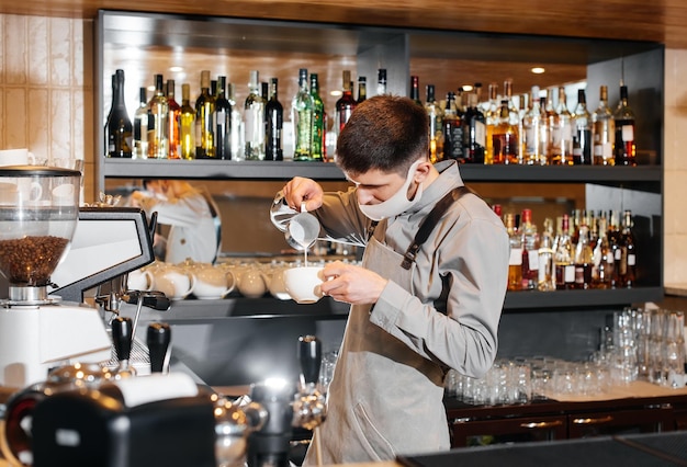 A masked barista prepares an exquisite delicious coffee at the bar in a coffee shop The work of restaurants and cafes during the pandemic