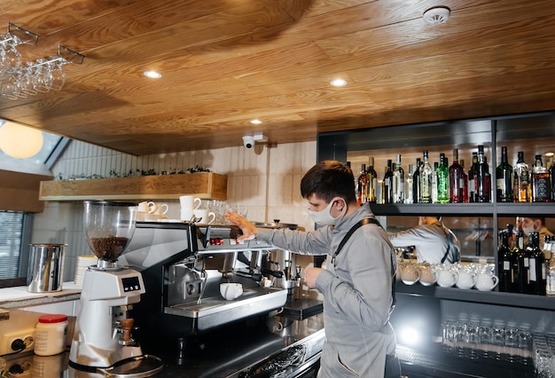 A masked barista prepares an exquisite delicious coffee at the bar in a coffee shop The work of restaurants and cafes during the pandemic