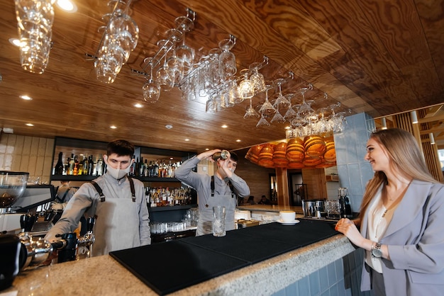 A masked barista prepares and serves delicious natural coffee to a young girl in a beautiful cafe during a pandemic