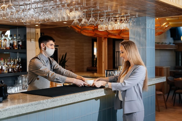 A masked barista prepares and serves delicious natural coffee to a young girl in a beautiful cafe during a pandemic