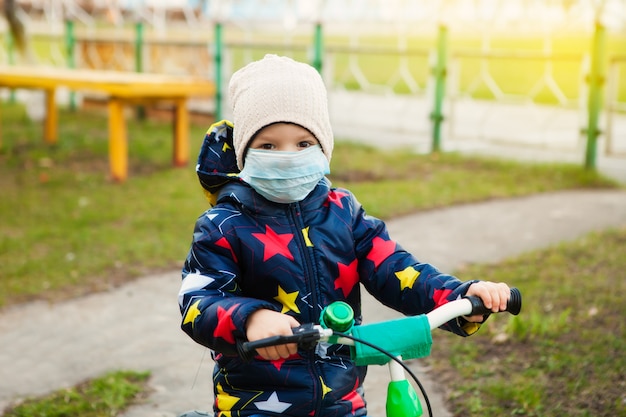 A masked child walks on the street, rides a bicycle, using all precautions to prevent coronavirus infection.