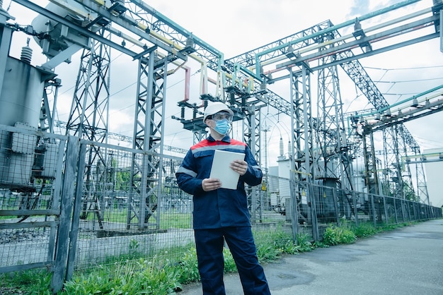 A masked power engineer during a pandemic inspects the modern equipment of an electrical substation before commissioning Energy and industry Scheduled repair of electrical equipment