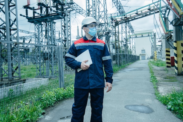 A masked power engineer during a pandemic inspects the modern equipment of an electrical substation before commissioning Energy and industry Scheduled repair of electrical equipment