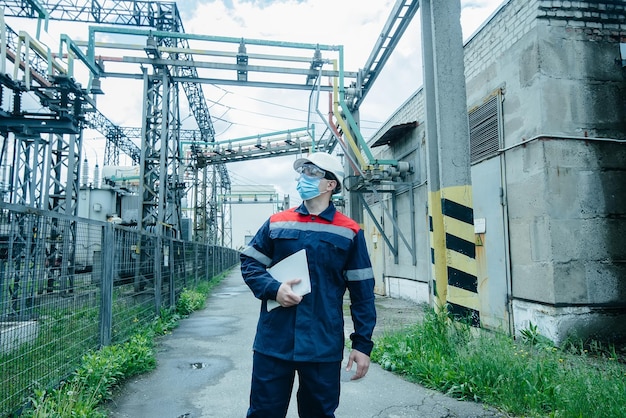 A masked power engineer during a pandemic inspects the modern equipment of an electrical substation before commissioning Energy and industry Scheduled repair of electrical equipment