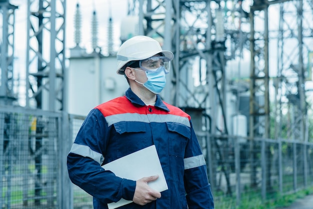 A masked power engineer during a pandemic inspects the modern equipment of an electrical substation before commissioning Energy and industry Scheduled repair of electrical equipment