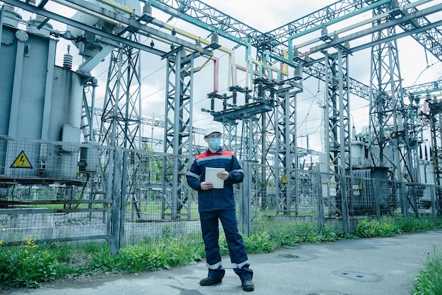 A masked power engineer during a pandemic inspects the modern equipment of an electrical substation before commissioning Energy and industry Scheduled repair of electrical equipment