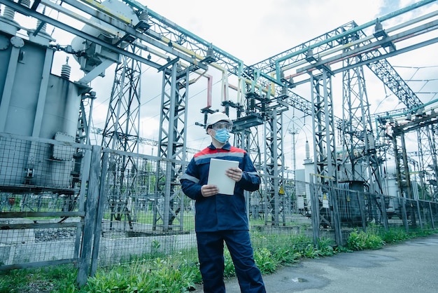 A masked power engineer during a pandemic inspects the modern equipment of an electrical substation before commissioning Energy and industry Scheduled repair of electrical equipment