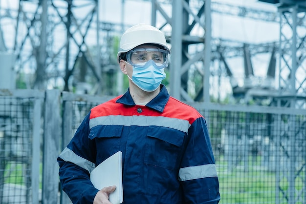 A masked power engineer during a pandemic inspects the modern equipment of an electrical substation before commissioning Energy and industry Scheduled repair of electrical equipment