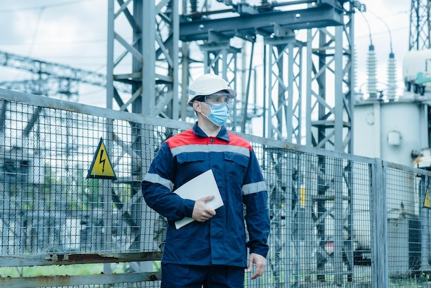 A masked power engineer during a pandemic inspects the modern equipment of an electrical substation before commissioning Energy and industry Scheduled repair of electrical equipment