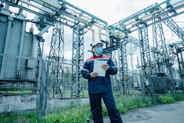 A masked power engineer during a pandemic inspects the modern equipment of an electrical substation before commissioning Energy and industry Scheduled repair of electrical equipment