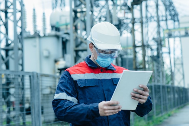 A masked power engineer during a pandemic inspects the modern equipment of an electrical substation before commissioning Energy and industry Scheduled repair of electrical equipment