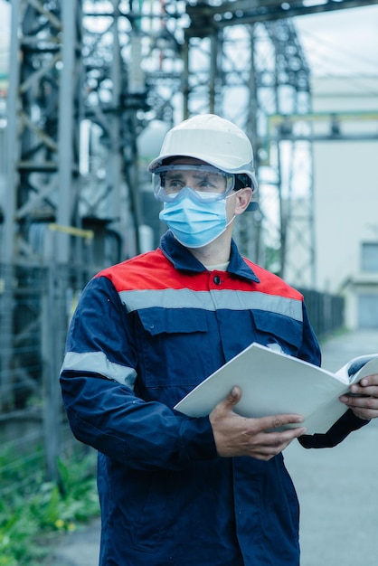 A masked power engineer during a pandemic inspects the modern equipment of an electrical substation before commissioning Energy and industry Scheduled repair of electrical equipment