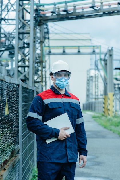 A masked power engineer during a pandemic inspects the modern equipment of an electrical substation before commissioning Energy and industry Scheduled repair of electrical equipment