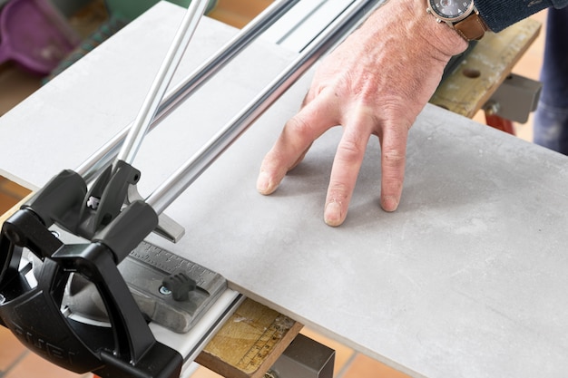 The mason cuts a ceramic tile with a tile cutter