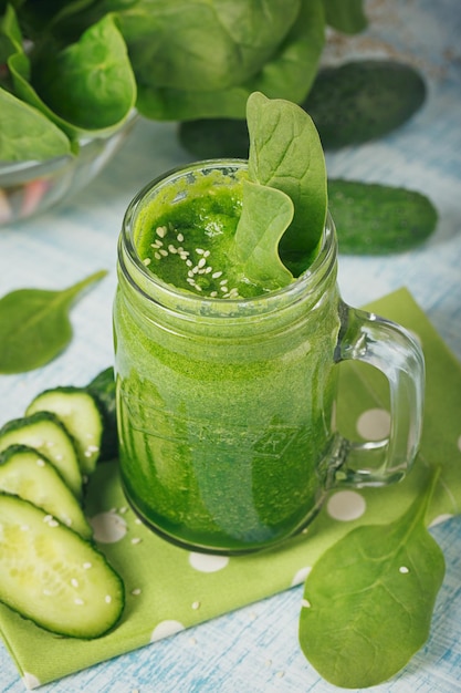 Mason jar mugs filled with fresh green spinach and cucumber smoothie on light blue wooden background. Healthy food and vegetarian concept.