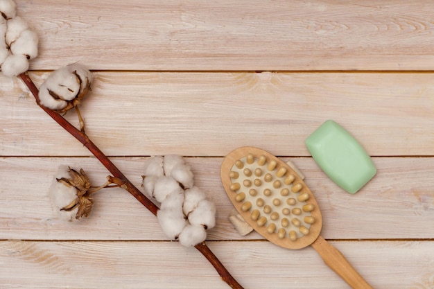 Massage brush and soap bar on light wooden table cotton flower closeup sponge