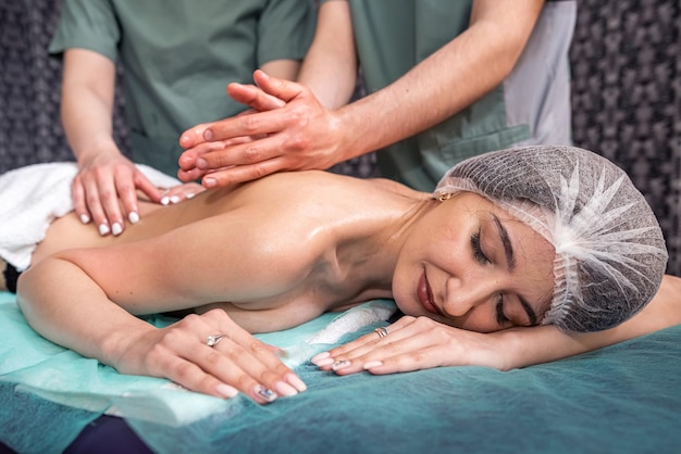 Massage in four hands over the patient's back is performed by two massage therapists a woman and a man at the same time effective therapeutic massage spa salon healthy body