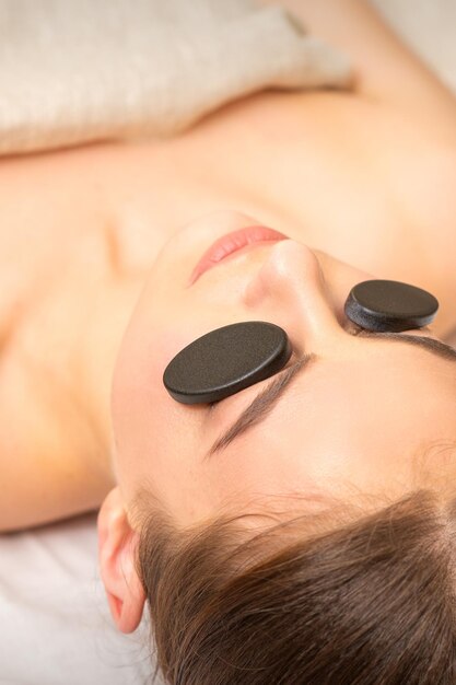 Massage with stones on the eyes of young woman getting a treatment in a beauty spa.