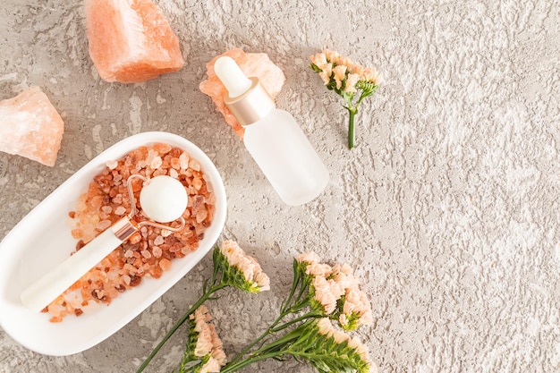 A massager made of white natural stone of round shape lies on sea salt in an oval bowl Cosmetic product for mvssage in a matte bottle copy space