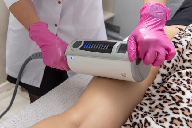 The masseur does a massage using anticellulite massage machine with compression and vibration technology in beautician office