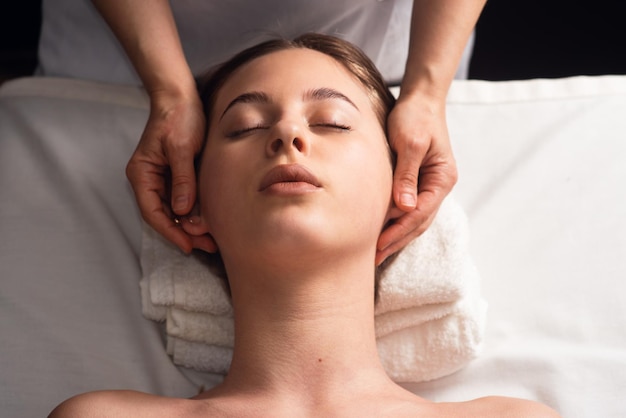 Masseur doing facial massage to young woman on massage table Concept of massage spa treatments Closeup