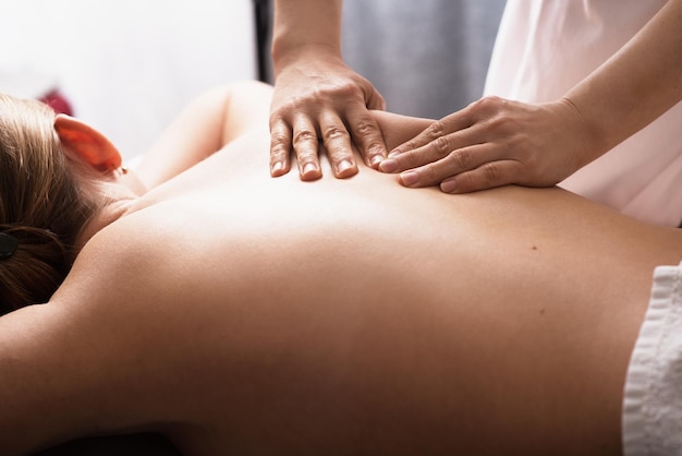 Masseur massaging back and shoulder blades of young woman on massage table Concept of massage spa treatments Closeup