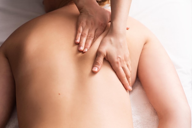 Masseur massaging back and shoulder blades of young woman on massage table Concept of massage spa treatments Closeup