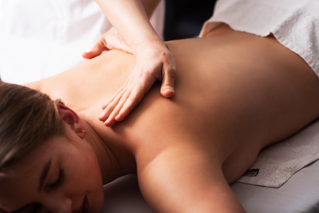 Masseur massaging back and shoulder blades of young woman on massage table Concept of massage spa treatments Closeup